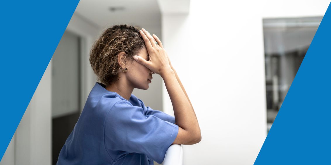 A young woman wearing scrubs is holding her head in distress.