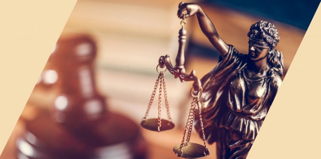 A bronze statue wearing a blindfold and holding a balance with a gavel in the background