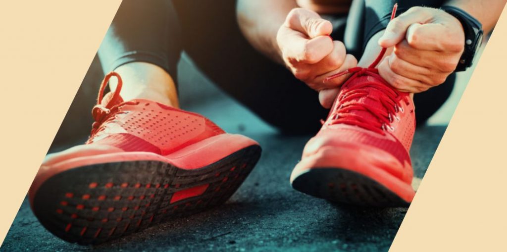 A close-up of a person sitting on the ground tying a pair of red shoes